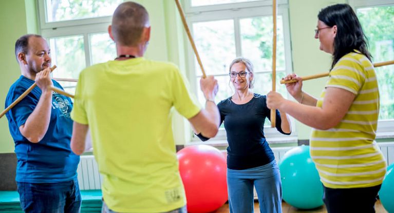 Drei Patieten und eine Therapeutin trainieren mit Stöcken in der Bewegungstherapie