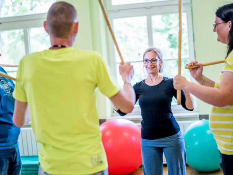 Drei Patieten und eine Therapeutin trainieren mit Stöcken in der Bewegungstherapie
