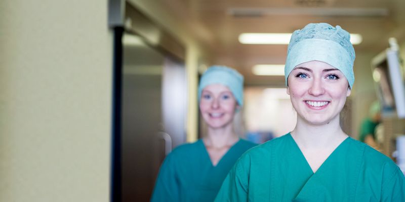 Zwei junge Frauen in grüner Pflegerkleidung lächeln in die Kamera