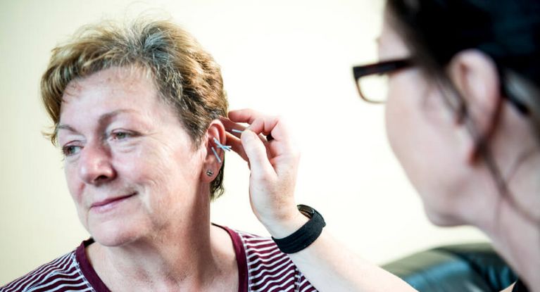 Ärztin setzt bei einer Patientin Akupunkturnadeln ans Ohr