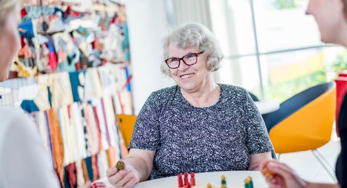 Zwei Therapeutinnen spielen mit einer alten Dame Mensch ärger Dich nicht.