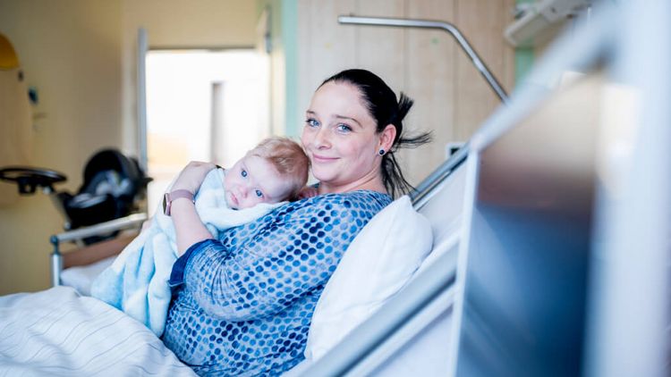 Junge, im Krankenbett liegende Mutter hält ihr neugeborenen Sohn im Arm.