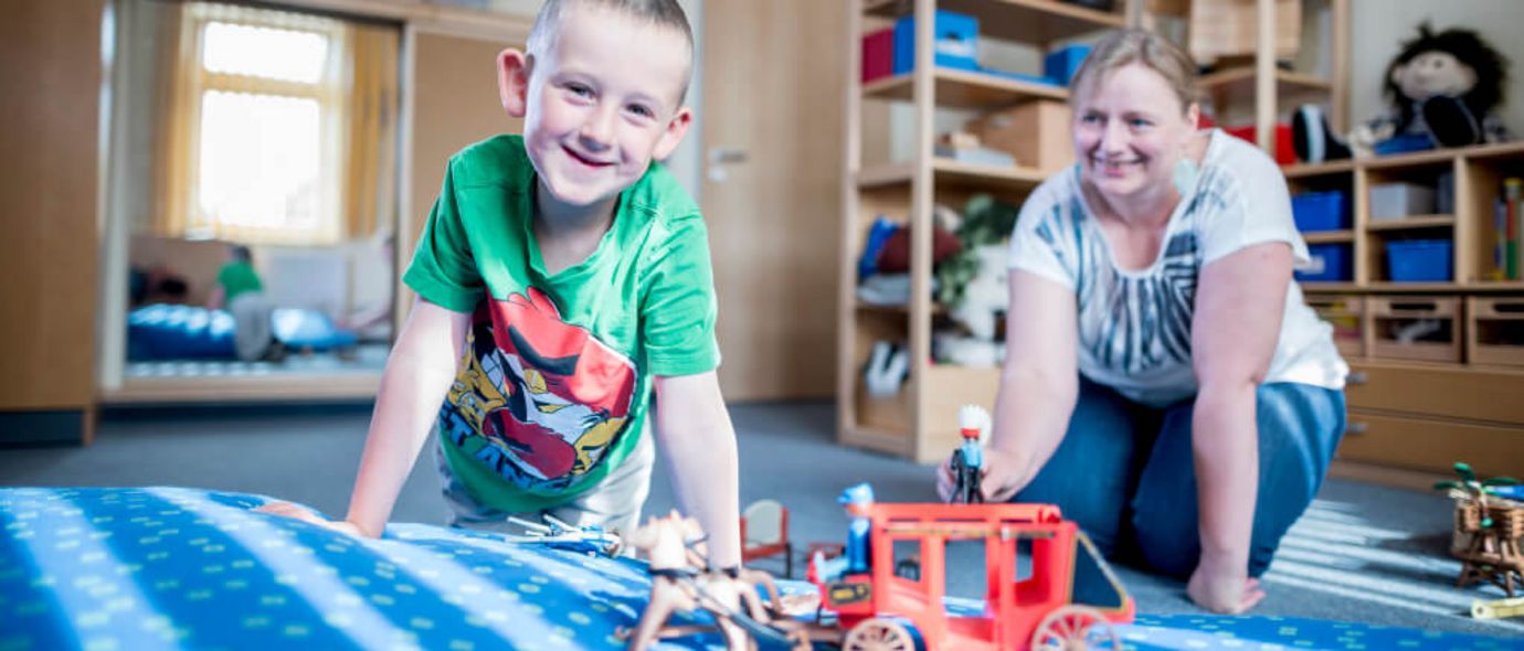 Junger Patient und Therapeutin spielen mit Playmobilpferden
