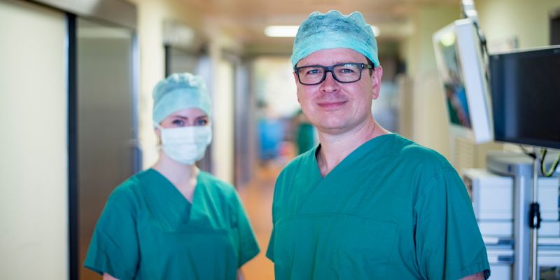 Arzt und eine Op-Pflegerin mit Mundschutz blicken in die Kamera
