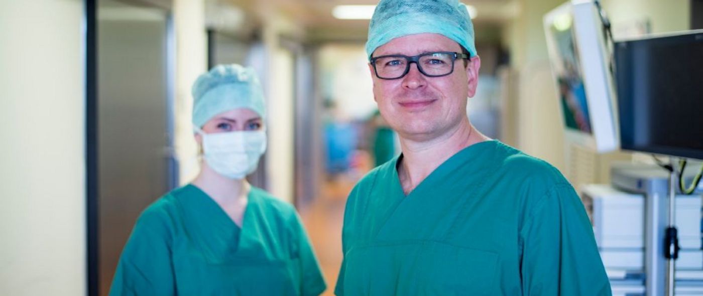 Arzt und eine Op-Pflegerin mit Mundschutz blicken in die Kamera