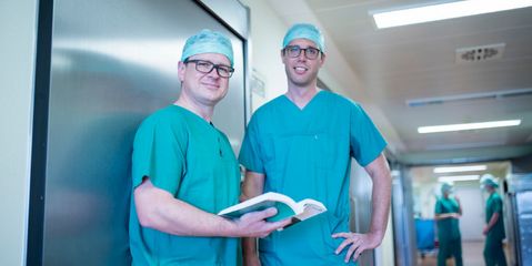 Zwei Ärzte in OP-Outfit lächeln in die Kamera