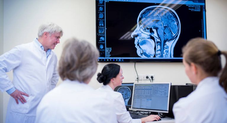 Ein Team aus Ärztinnen und Ärzten bespricht gemeinsam das Röntgenbild einen menschlichen Kopfes
