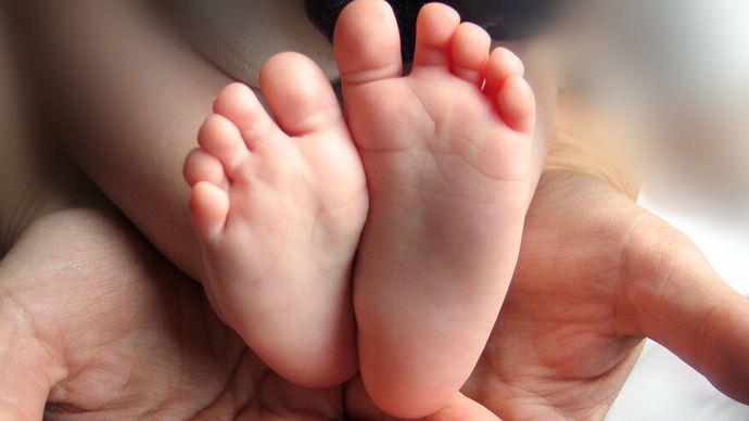 Zwei erwachene Hände halten die beiden Füße eines Neugeborenen