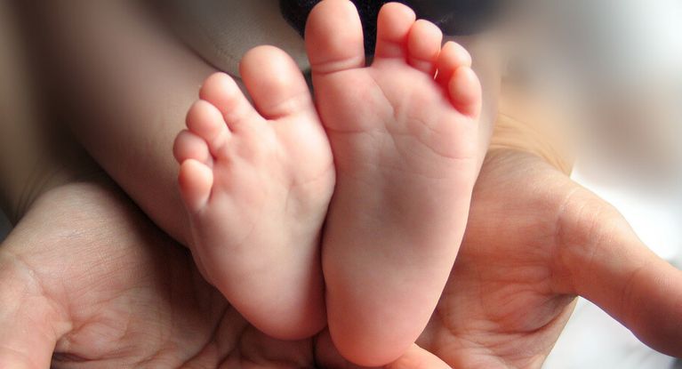 Zwei erwachene Hände halten die beiden Füße eines Neugeborenen