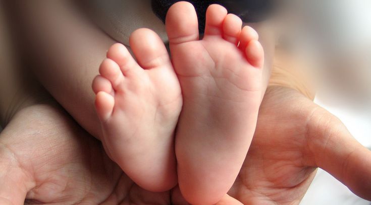 Eine erwachsene Hand hält kleine Füße eines Neugeborenen