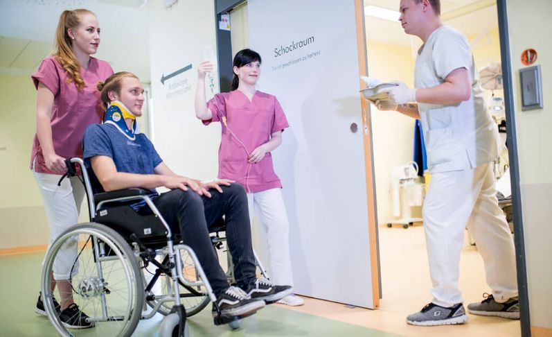 Pflegerinnen schieben einen jungen Patienten im Rollstuhl in den Schockraum