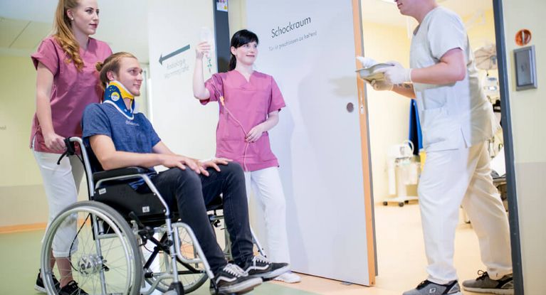 Pflegerinnen schieben einen jungen Patienten im Rollstuhl in den Schockraum