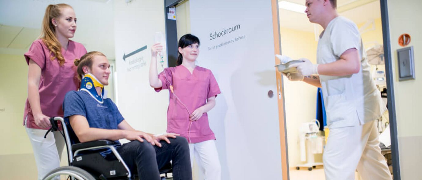 Pflegerinnen schieben einen jungen Patienten im Rollstuhl in den Schockraum