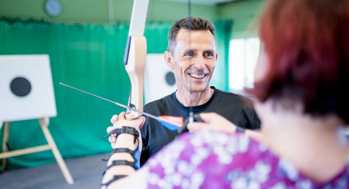 Patientin und Therapeut beim Bogenschießen in der Sporthalle
