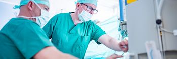 Zwei Anästhesisten in Kasack und mit Mundschutz überwachen eine Operation.