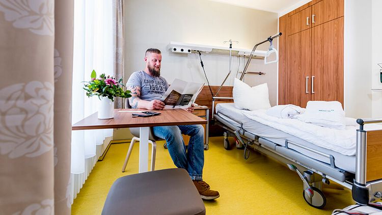 Ein bärtiger Patient liest die Speisekarte in einem Privita-Zimmer im MEDICLIN Müritz-Klinikum