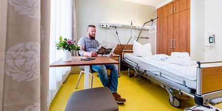 Ein bärtiger Patient liest die Speisekarte in einem Privita-Zimmer im MEDICLIN Müritz-Klinikum