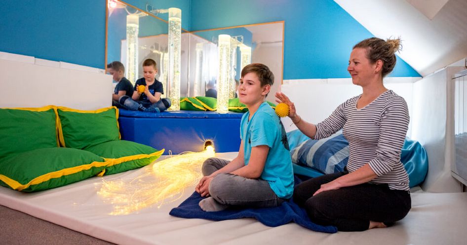 Im Entspannungsraum massiert eine Therapeutin einen jungen Patienten mit einem gelben Igelball