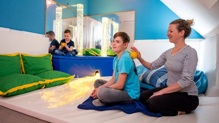 Im Entspannungsraum massiert eine Therapeutin einen jungen Patienten mit einem gelben Igelball
